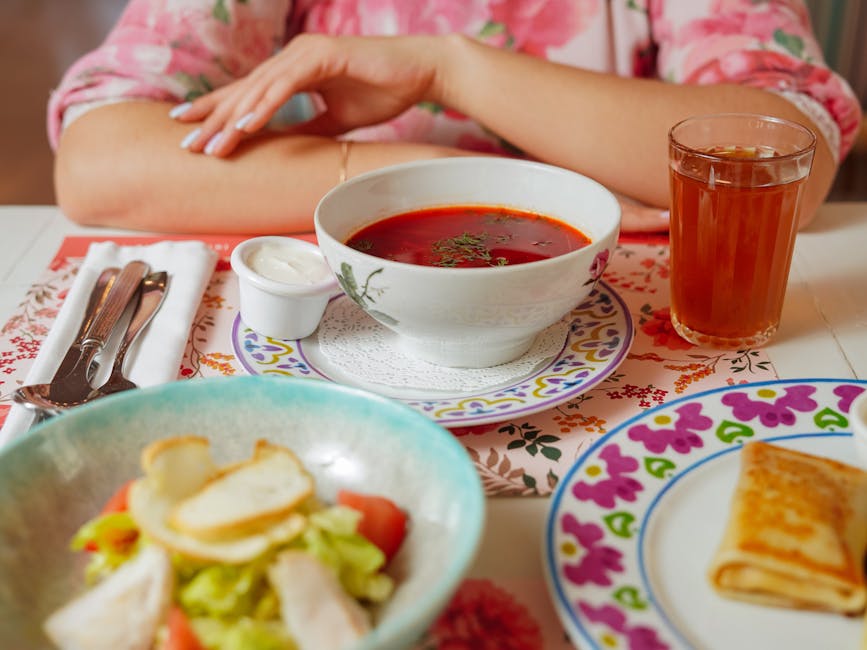 A bowl of red borsch soup topped with sour cream, fresh dill, and rye bread on the side