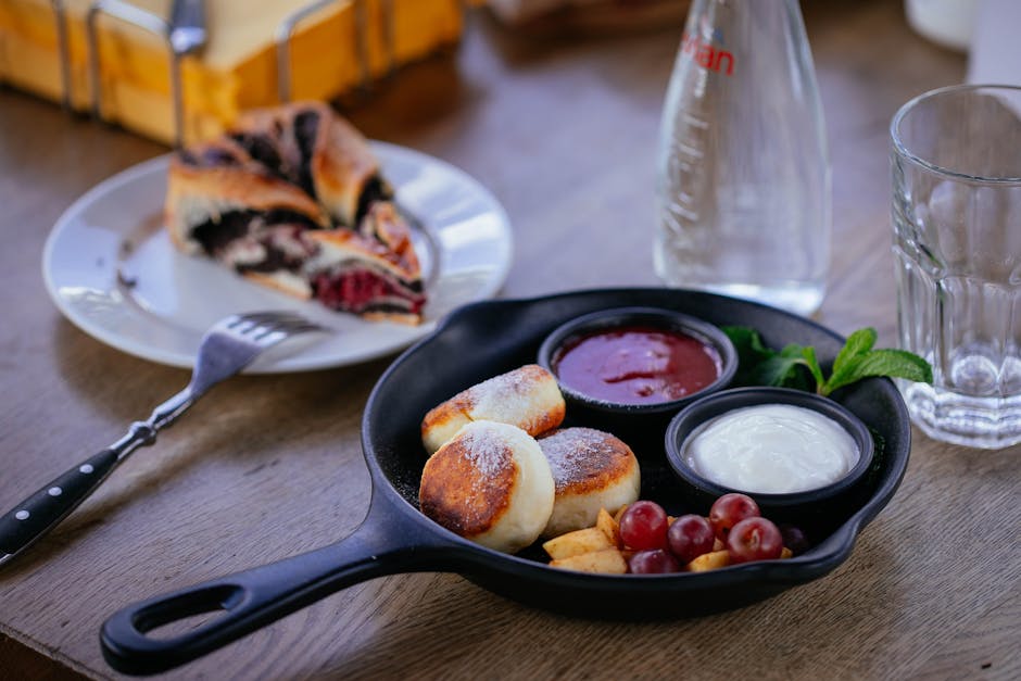Golden fried syrniki cheese pancakes stacked on a plate with sour cream and berry jam