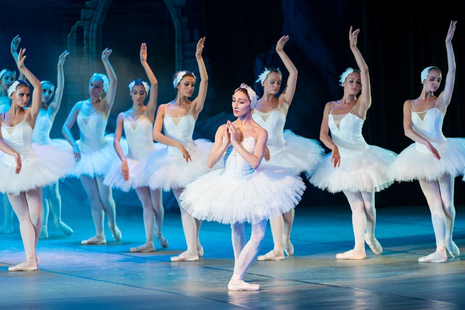 Elegant ballerinas in classic white tutus performing Swan Lake on a theatre stage under soft lighting